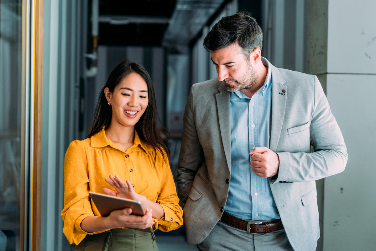 man and woman walking through hallway chatting and looking at notes